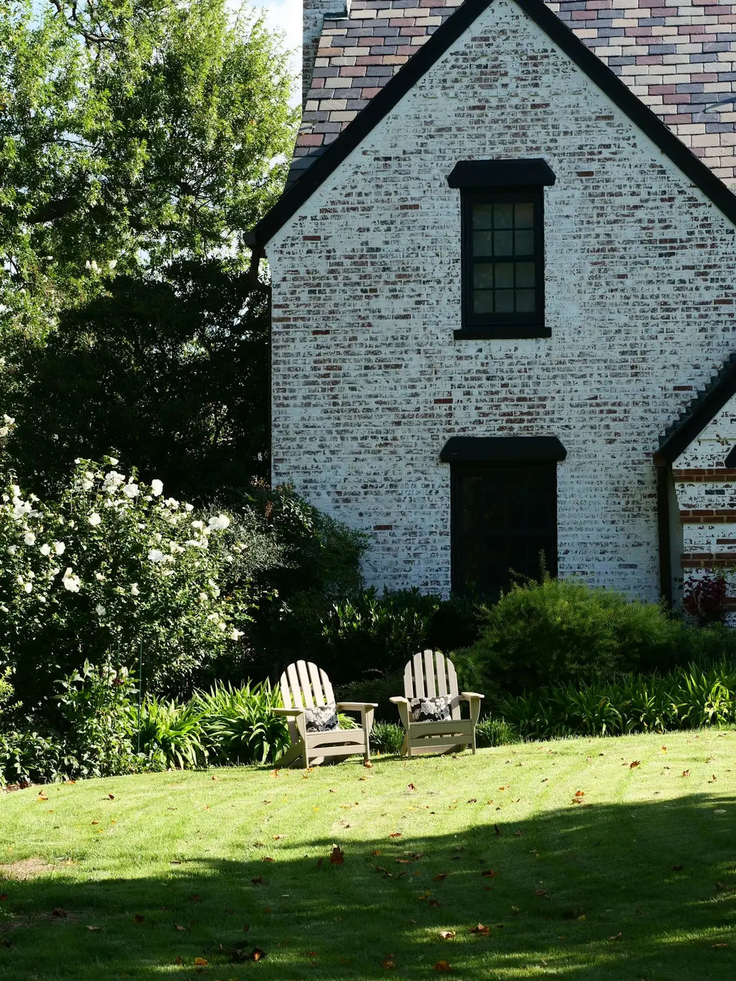 Wit bakstenen huis met een verzorgd gazon, borders en twee tuinstoelen