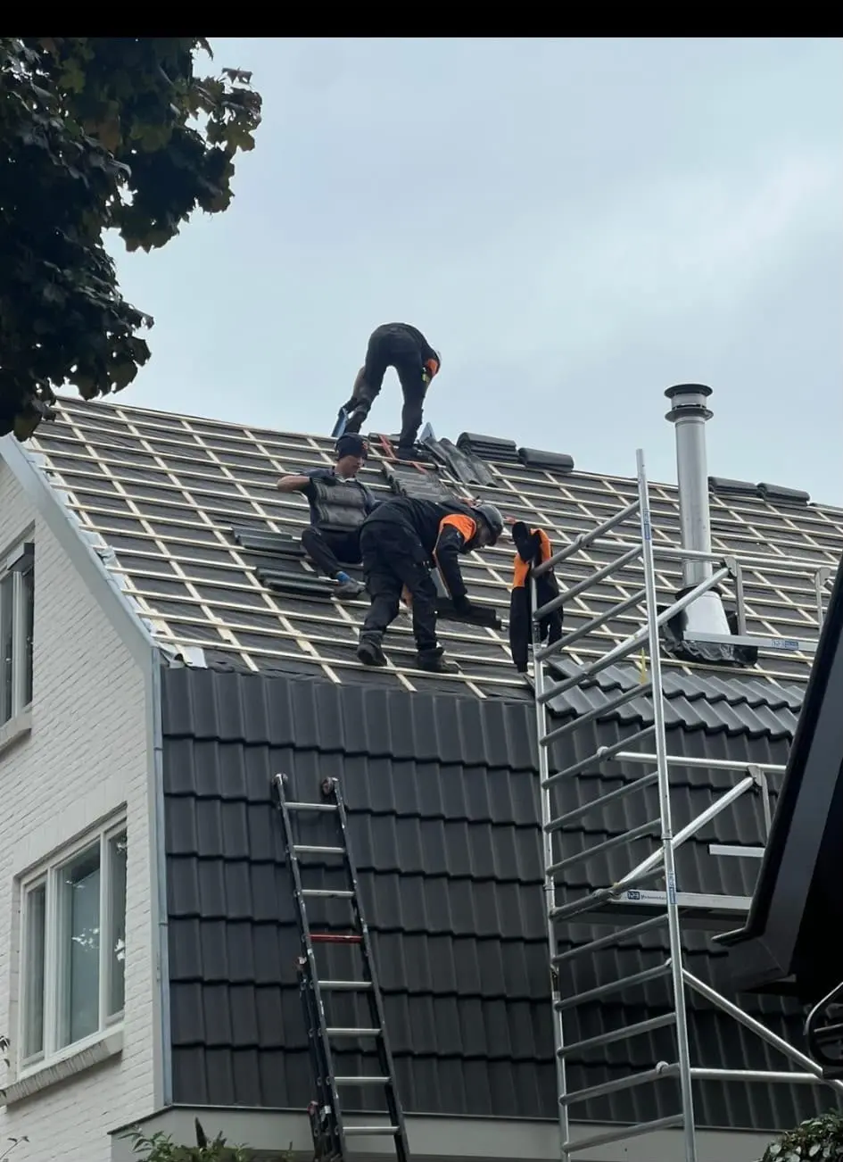 Het team legt nieuwe panlatten en dakpannen op een pannendak, met rolsteiger ernaast
